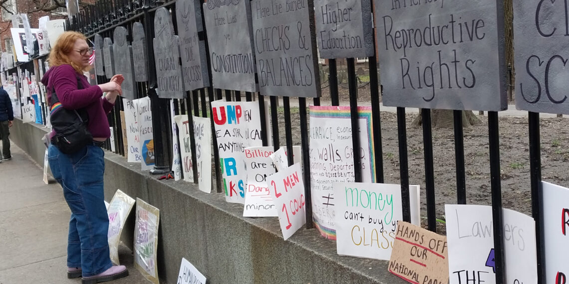 AME5885. BOSTON (ESTADOS UNIDOS), 05/04/2025.- Una mujer observa algunos carteles durante una protesta denominada 'Hands Off' este sábado, en Boston (Estados Unidos). Miles de personas participaron este sábado en protestas convocadas en un millar de ciudades y municipios de Estados Unidos, como Washington y Nueva York, en contra de los recortes y otras políticas del presidente, Donald Trump, a quien acusan de autoritario. EFE/ Iñaki Estívaliz