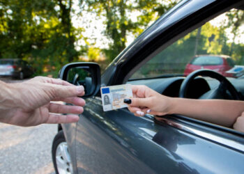 Teenager driver commited a minor offence and handing over her licence to a police officer reaching towards the open window.Police officer controlling traffic on the road