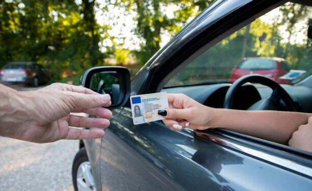 Teenager driver commited a minor offence and handing over her licence to a police officer reaching towards the open window.Police officer controlling traffic on the road