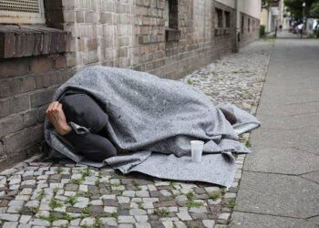 Homeless Man Covered With Blanket Sleeping On Street In City
