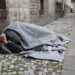 Homeless Man Covered With Blanket Sleeping On Street In City