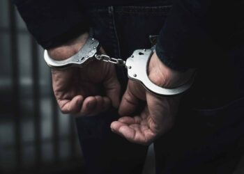 arrested man with cuffed hands behind prison bars